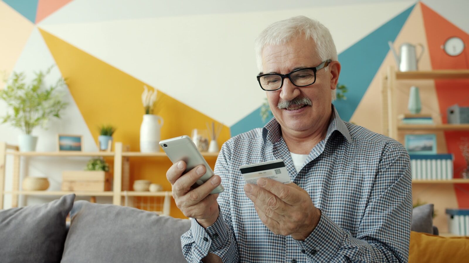 Elderly man uses smartphone and credit card for online shopping.
