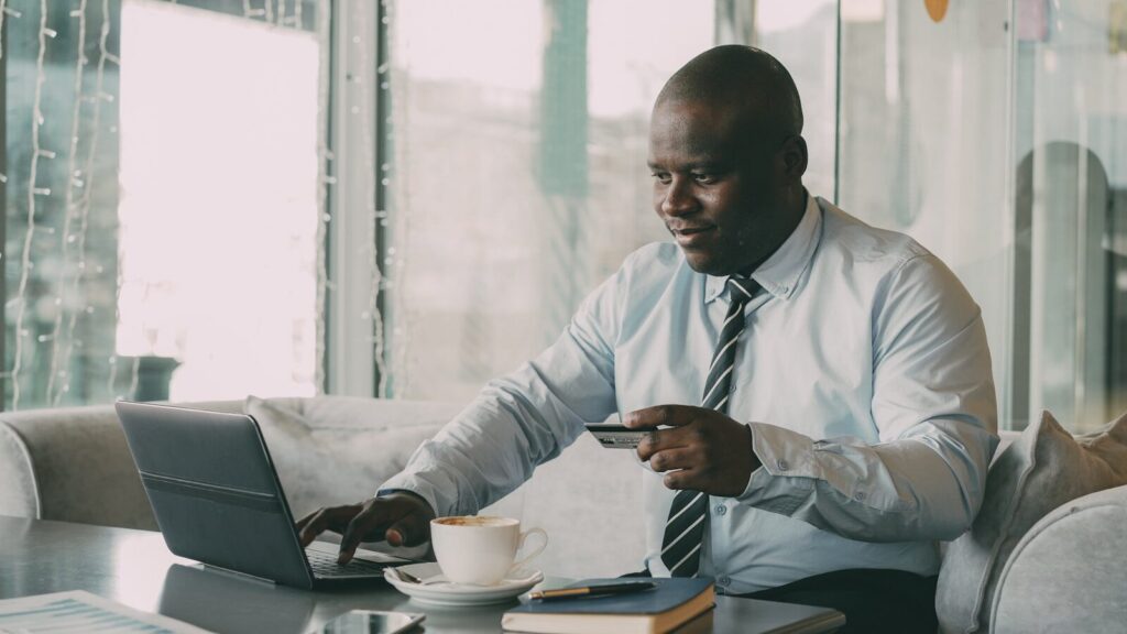 Man in shirt and tie using laptop and credit card.