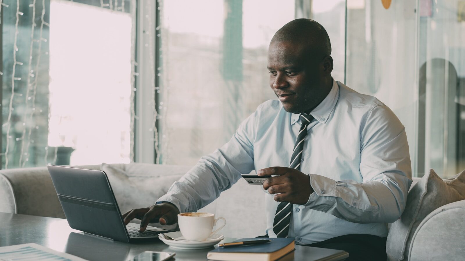 Man in shirt and tie using laptop and credit card.