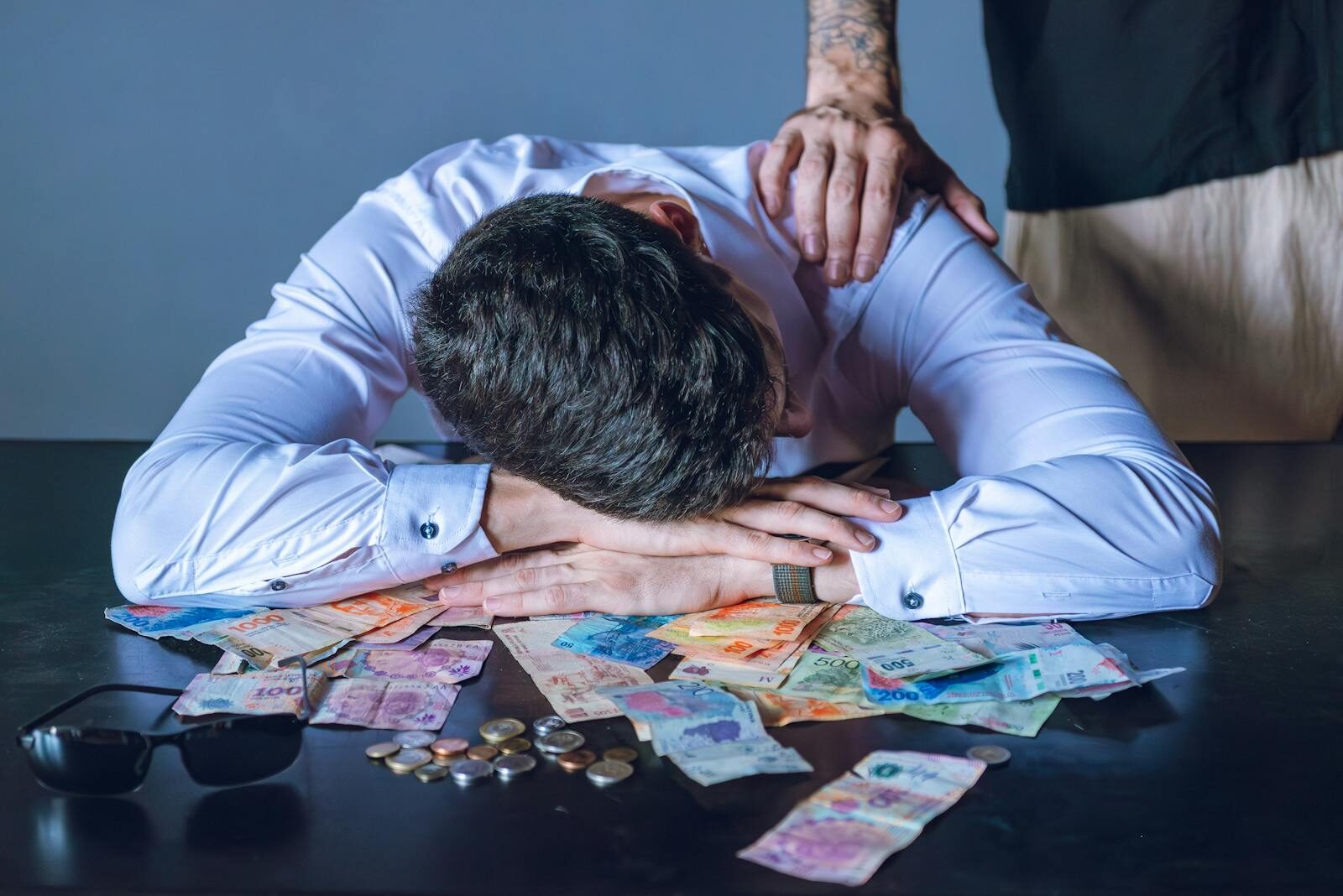 Stressed businessman rests on table with Argentine pesos in Buenos Aires.