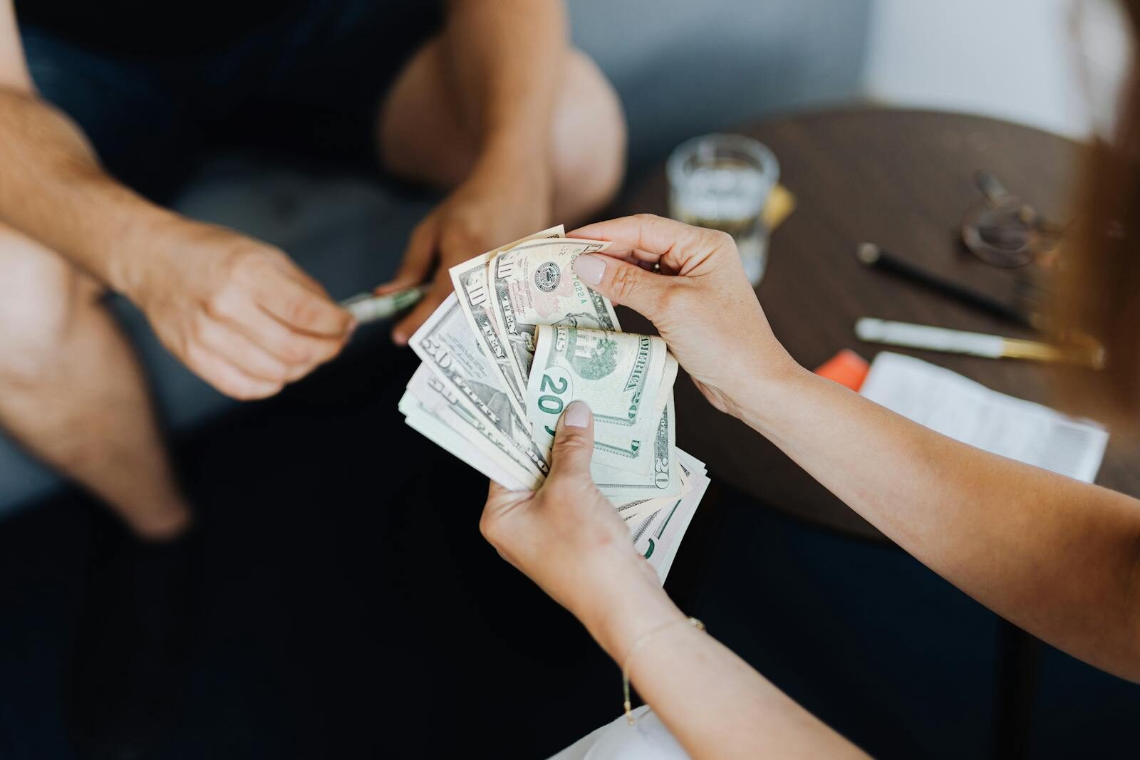 Close-up of people handling and counting US dollar bills indoors.