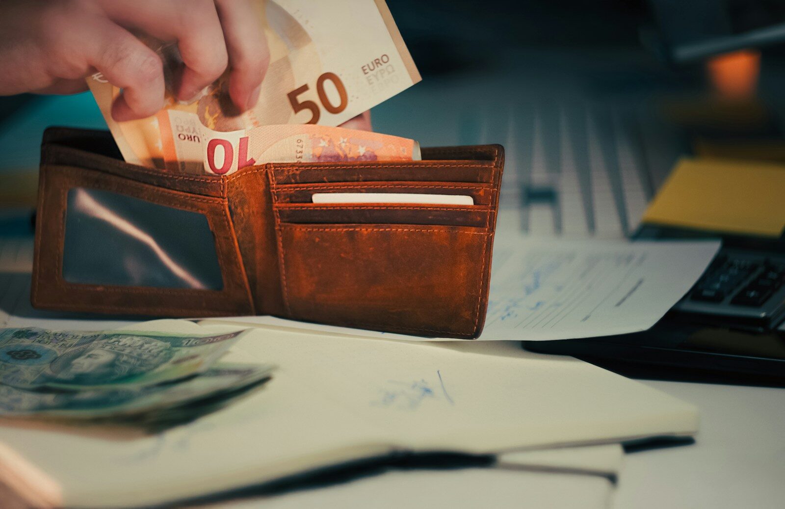 Hand placing euro banknotes into a brown leather wallet