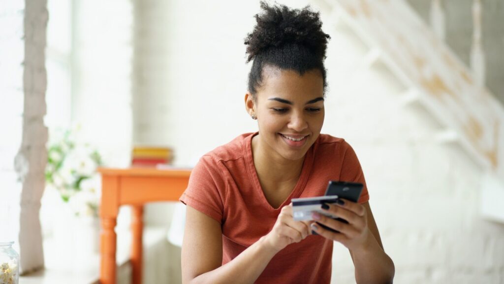 Young woman smiling while holding credit card and phone
