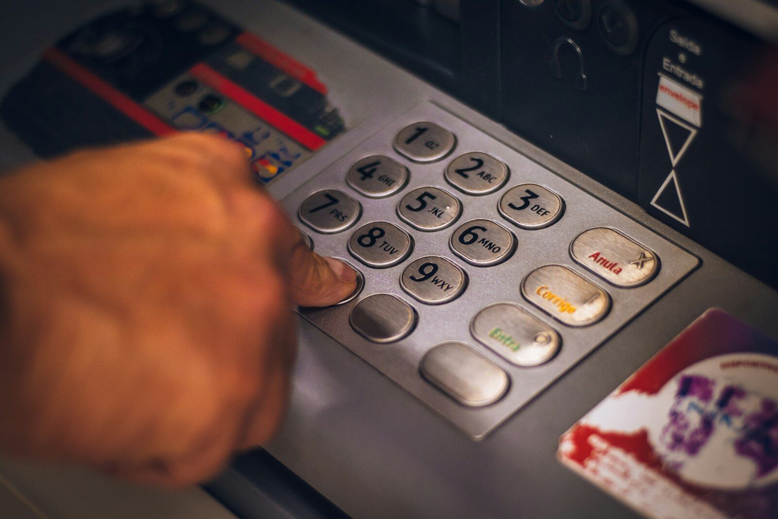 A person pressing a button on a metallic ATM keypad