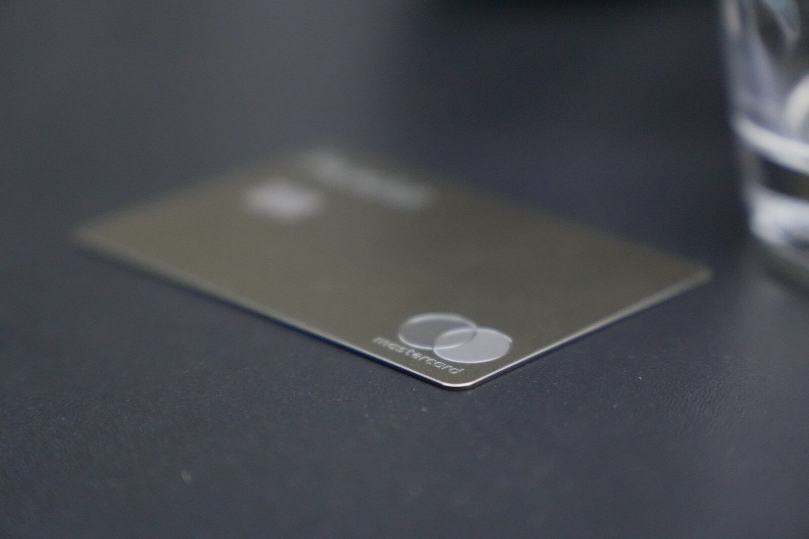 A grey credit card with a Mastercard logo on a dark surface